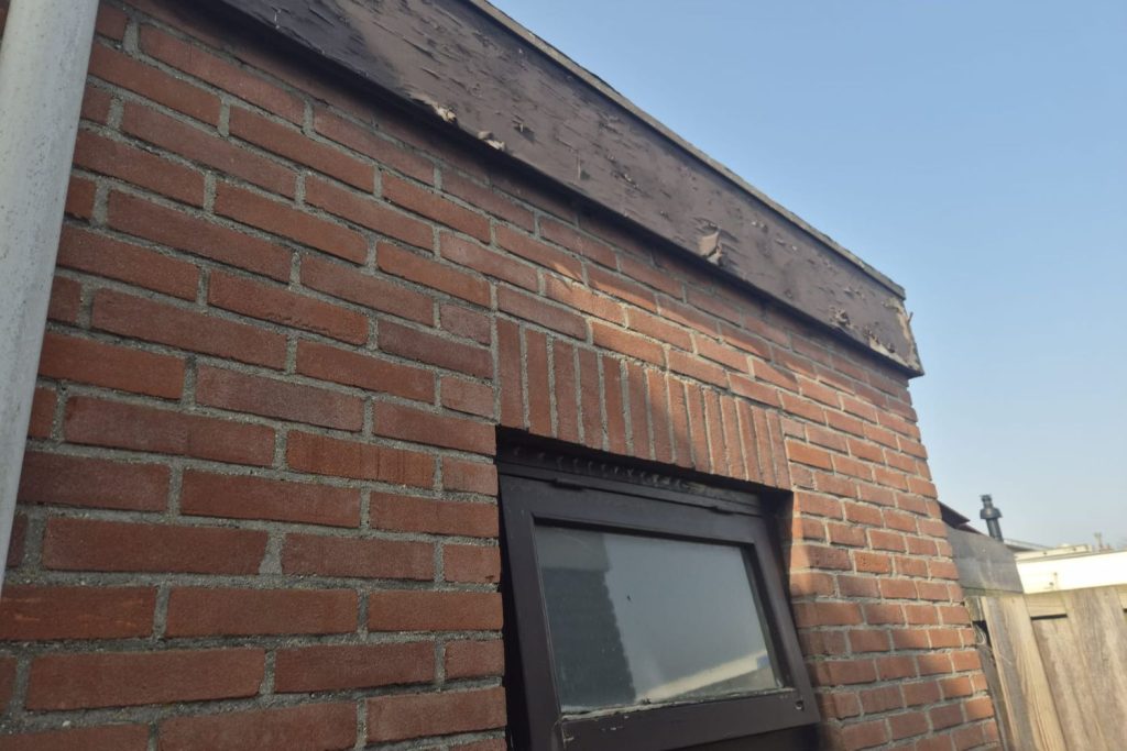 Bakstenen muur met raam en afbladderende verf bovenaan.